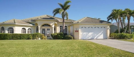 A two-story house with a garage, a well-maintained lawn, and palm trees.