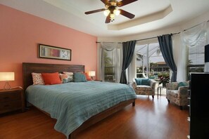 Ein Schlafzimmer mit einem Bett, einem Deckenventilator, einem Nachttisch, einem Sessel und einem Fernseher.