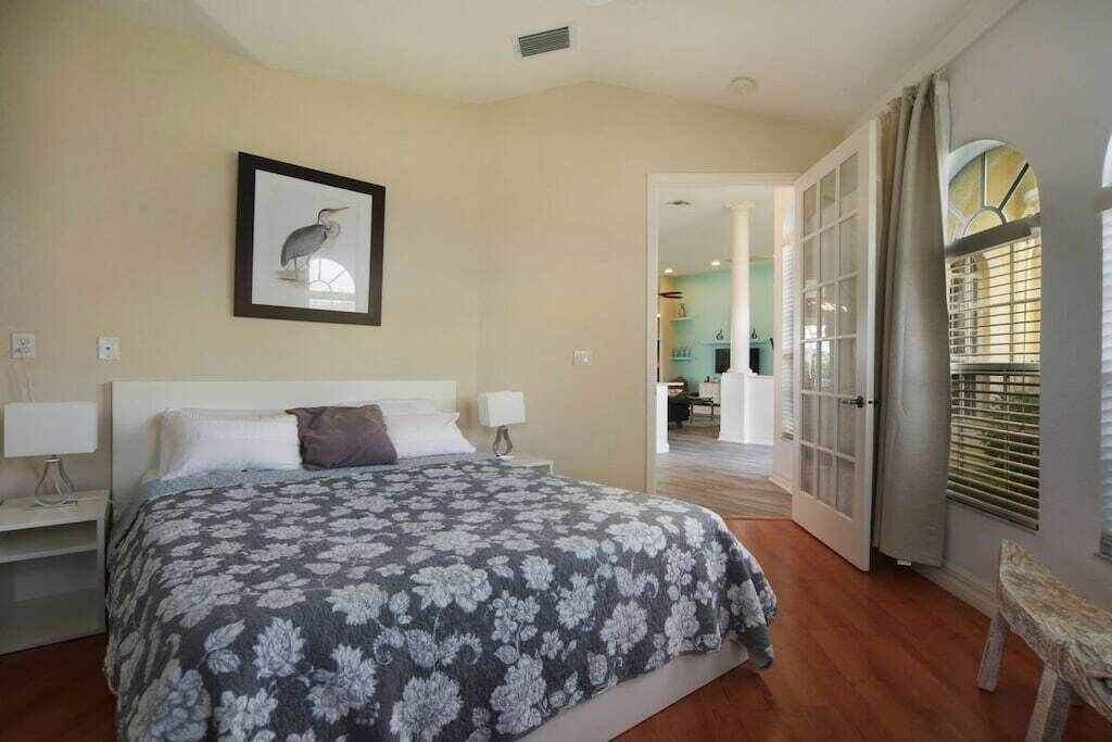 Un dormitorio con cama, mesitas de noche, un cuadro enmarcado en la pared y una puerta abierta que da a otra habitación.