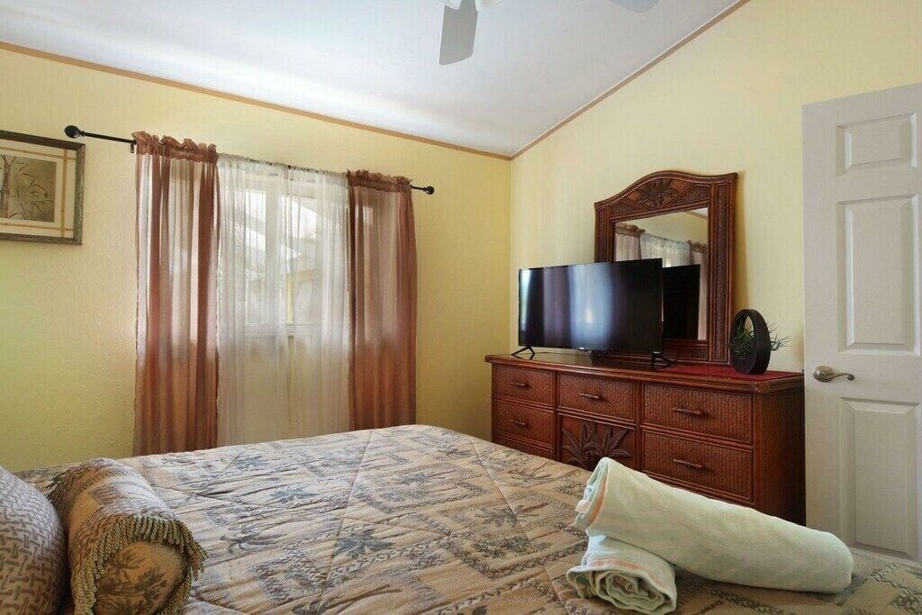Ein Schlafzimmer mit einem Bett, einem Fernseher auf einer Holzkommode, einer Tür und einem Fenster mit Vorhängen.