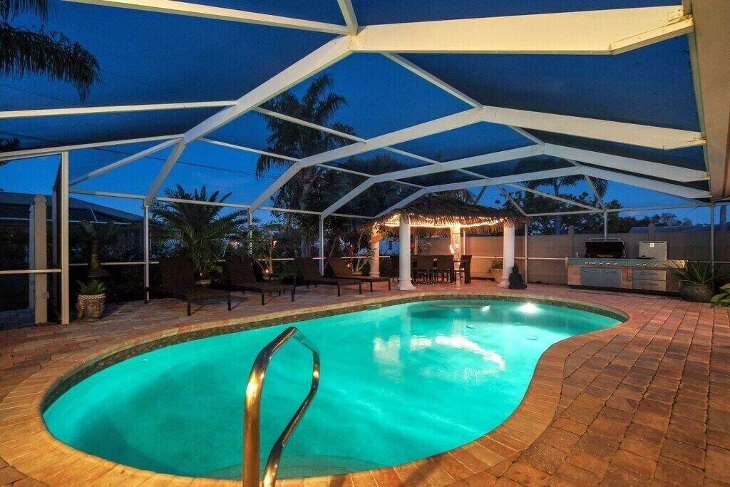 A swimming pool with a sunken center, surrounded by a covered patio area with chairs and a barbecue setup.