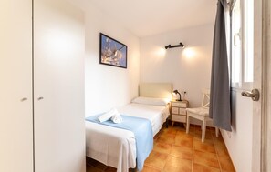 A small, well-lit bedroom with two beds, a bedside table with a lamp, a painting on the wall, and a window with curtains. - Awesome apartment in Arta with WiFi (Arta)