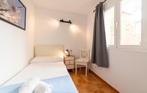 Quarto com cama, mesa de cabeceira, cadeira e janela com cortinas.