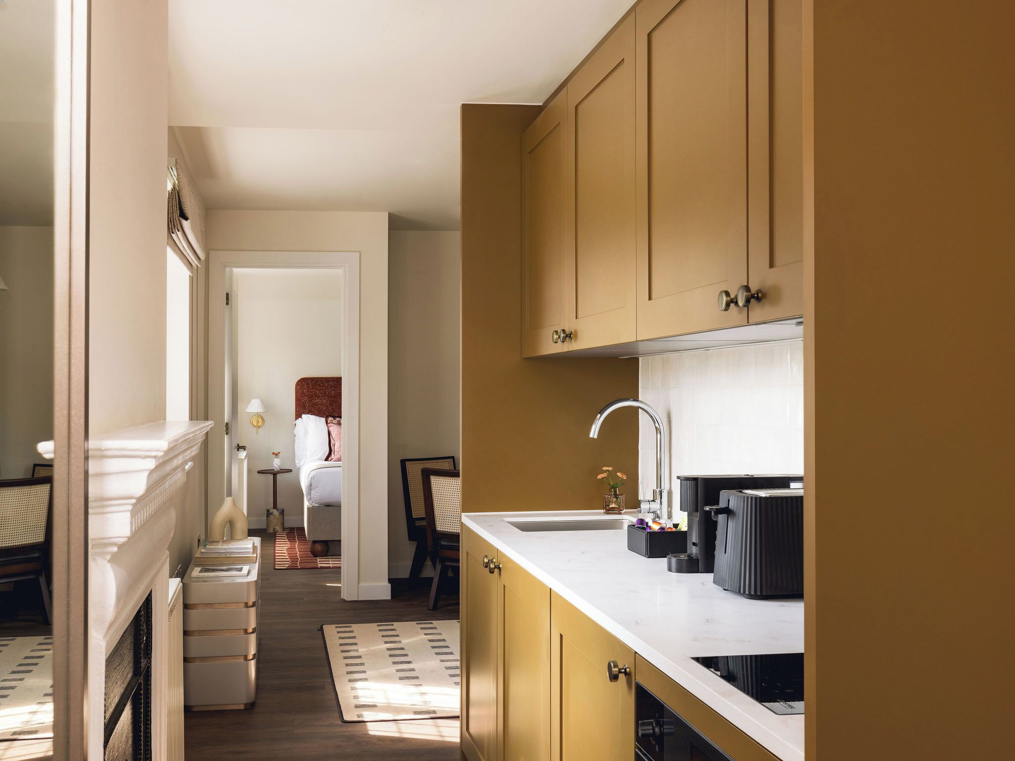 Cocina con encimera blanca, un lavamanos y armarios. Se ve una zona de comedor con una mesa y sillas a través de una puerta abierta.
