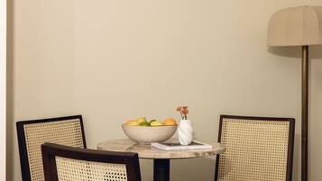 A dining table with a bowl of fruit and a vase with flowers, flanked by two chairs with woven backs.