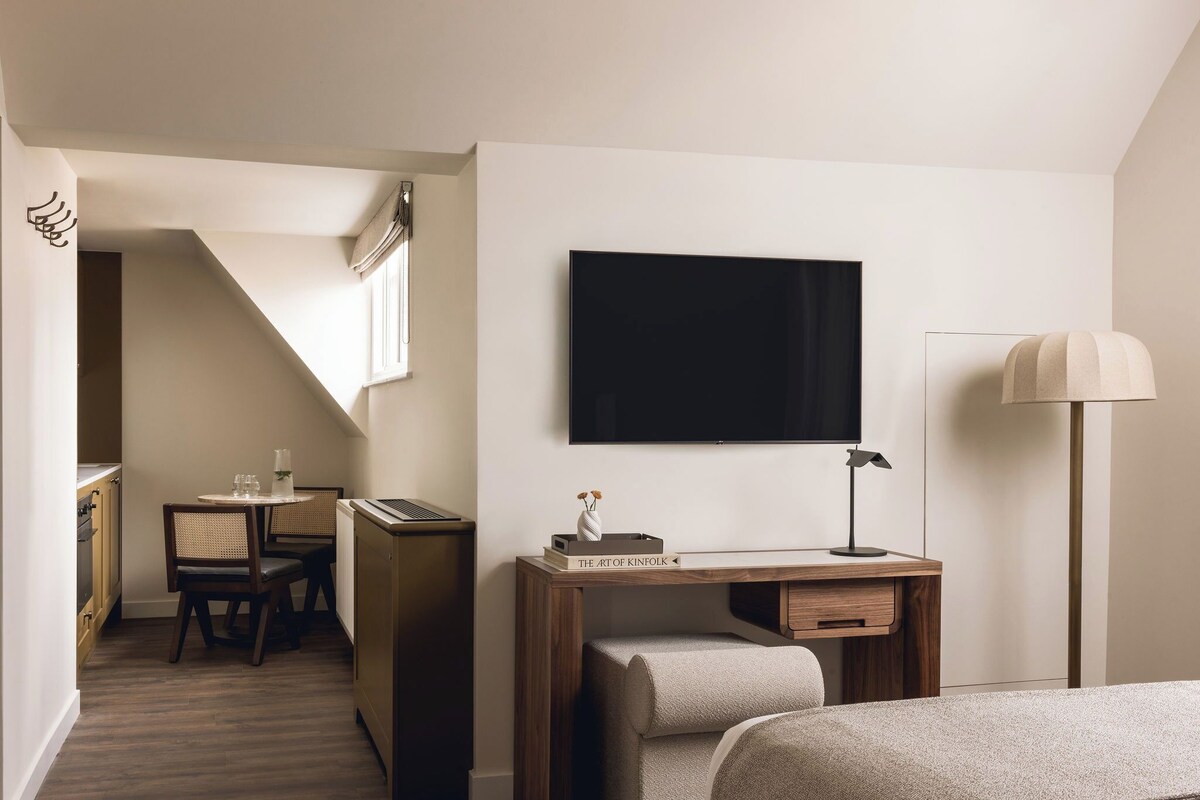 Una habitación de hotel con una cama, un escritorio con televisor de pantalla plana, una lámpara y un área de comedor con mesa y sillas.
