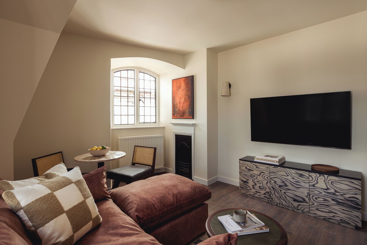 Una sala de estar moderna con sofá, una mesa de centro, chimenea, televisor y ventana con vistas.