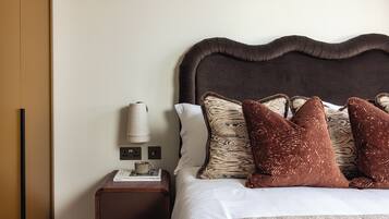 A neatly made bed with a dark headboard, a bedside table with a lamp, and a power outlet.