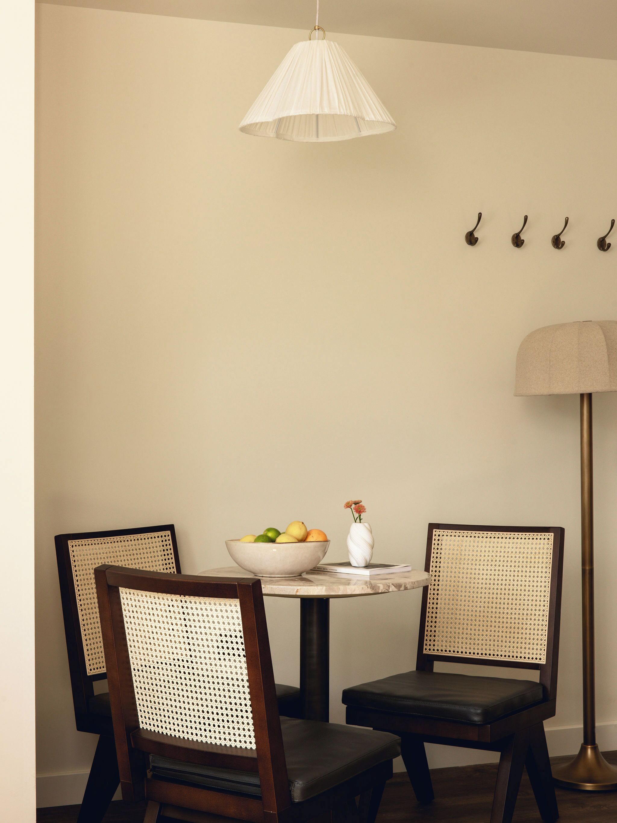 Een eethoek met een ronde tafel, twee stoelen, een fruitschaal, een vaas met bloemen en een hanglamp.