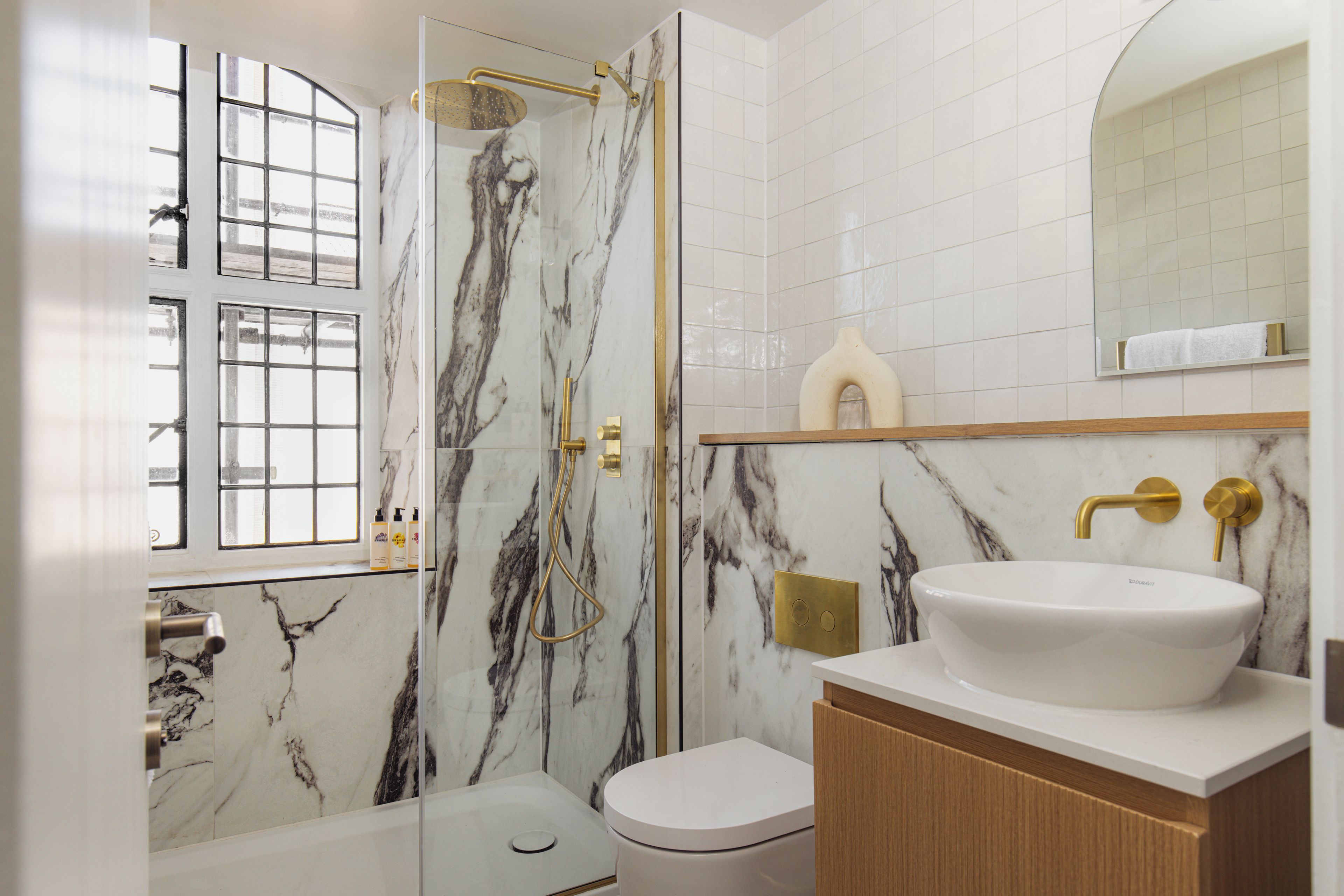 Ein Badezimmer mit einem weißen Waschbecken, Marmorwänden, einer Dusche mit goldfarbenen Armaturen und einer Toilette.