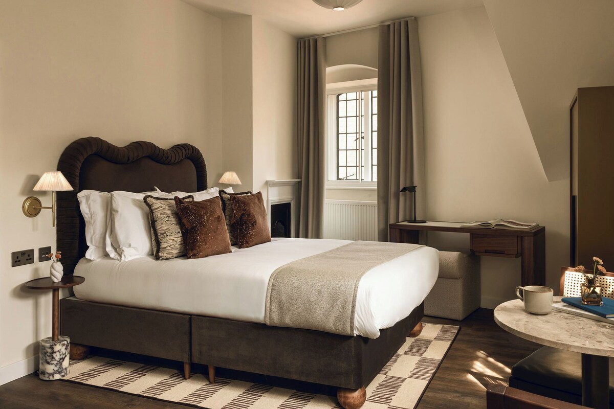 Un dormitorio moderno con una cama grande, lámparas de noche, un escritorio y una ventana con cortinas.