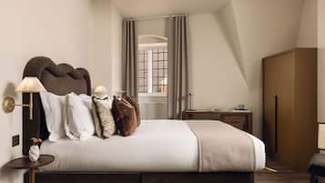 A modern bedroom with a large bed, bedside lamps, a window with curtains, a wooden wardrobe, and a small table with a book and cup.