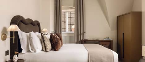 A modern bedroom with a large bed, bedside lamps, a window with curtains, a wooden wardrobe, and a small table with a book and cup.
