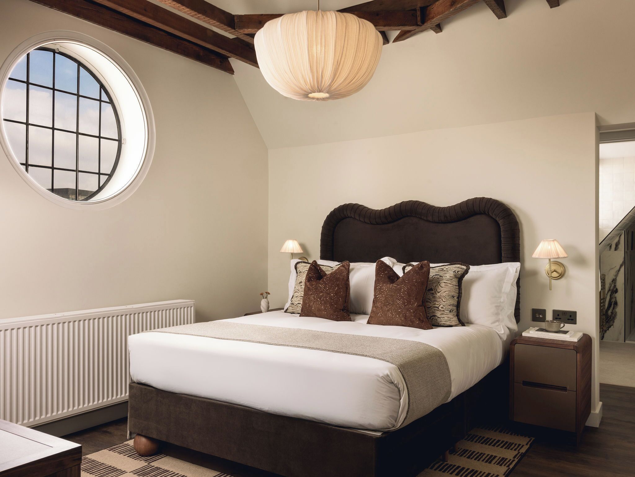 Un dormitorio con una cama grande, un ventanal redondo y una viga de techo de madera.
