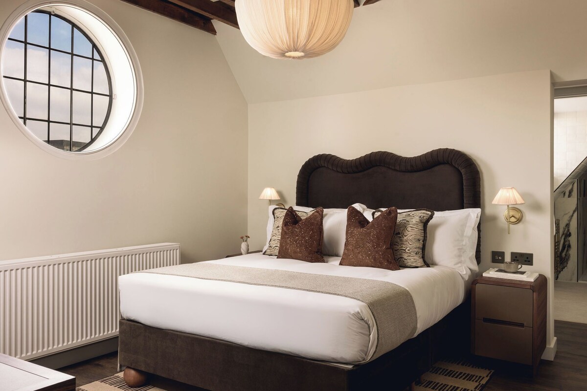 Un dormitorio con una cama grande, un ventanal redondo y una viga de techo de madera.