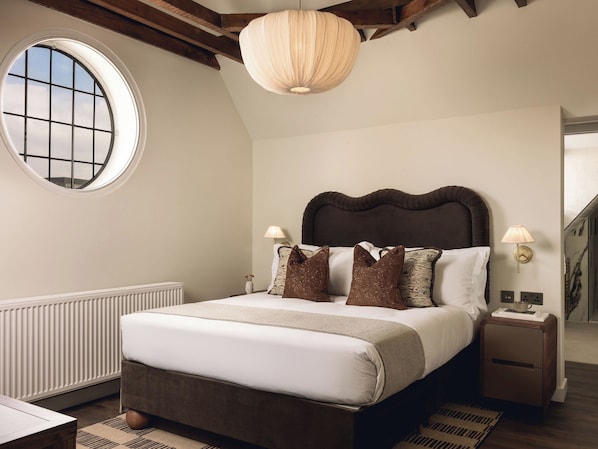 Un dormitorio con una cama grande, un ventanal redondo y una viga de techo de madera.