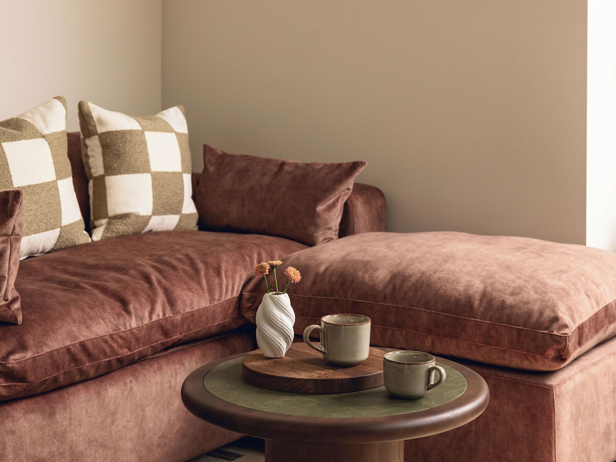 A cozy room with a brown sofa, a round wooden table, and a vase with flowers.
