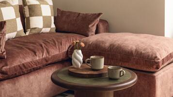 A cozy room with a brown sofa, a round wooden table, and a vase with flowers.