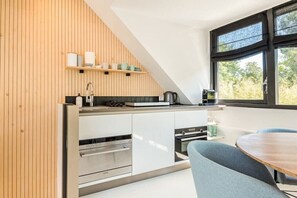 Une cuisine moderne dotée d’appareils électroménagers intégrés, d’un mur d’accent en bois et d’un coin repas avec une table et des chaises.