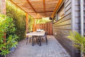 An outdoor patio with a wooden table and chairs, surrounded by plants and a wooden fence. - Holiday home in Alkmaar with barbecue (Alkmaar)