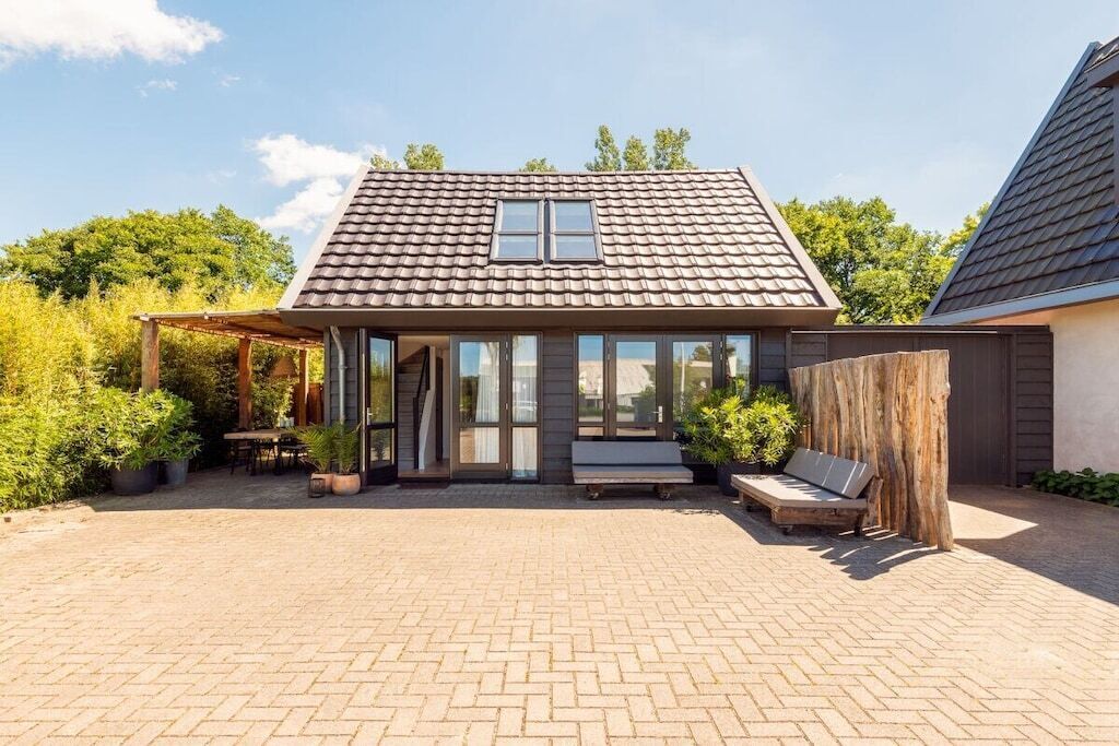 Ein Haus mit einem Ziegeldach, einer überdachten Terrasse mit Sitzgelegenheiten und einem Holzzaun.