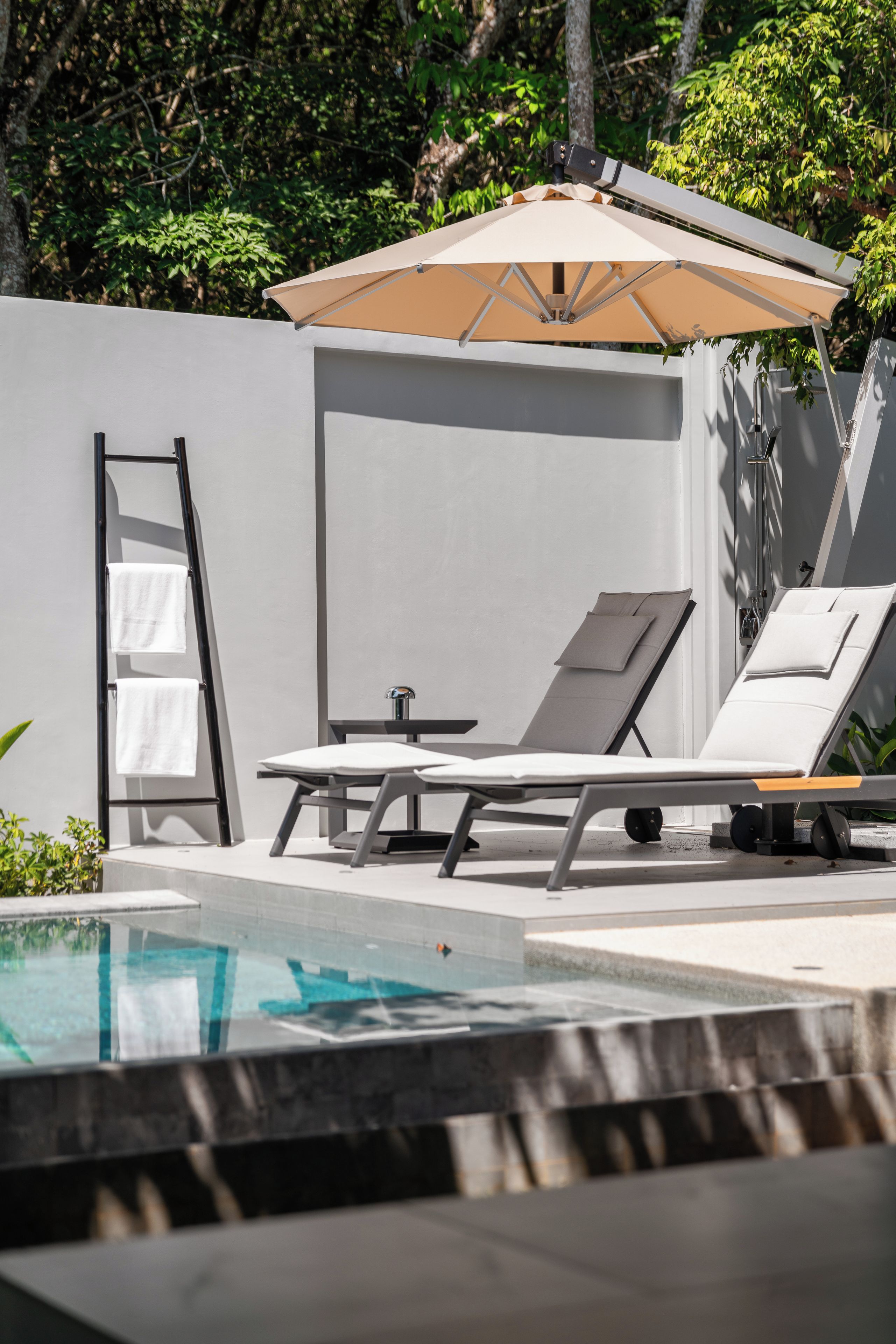 A modern outdoor pool area with two lounge chairs, a small table, and a ladder.
