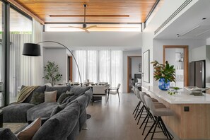 Un salon moderne avec un canapé gris, un coin repas avec une table dressée pour quatre personnes et une cuisine avec un bar.