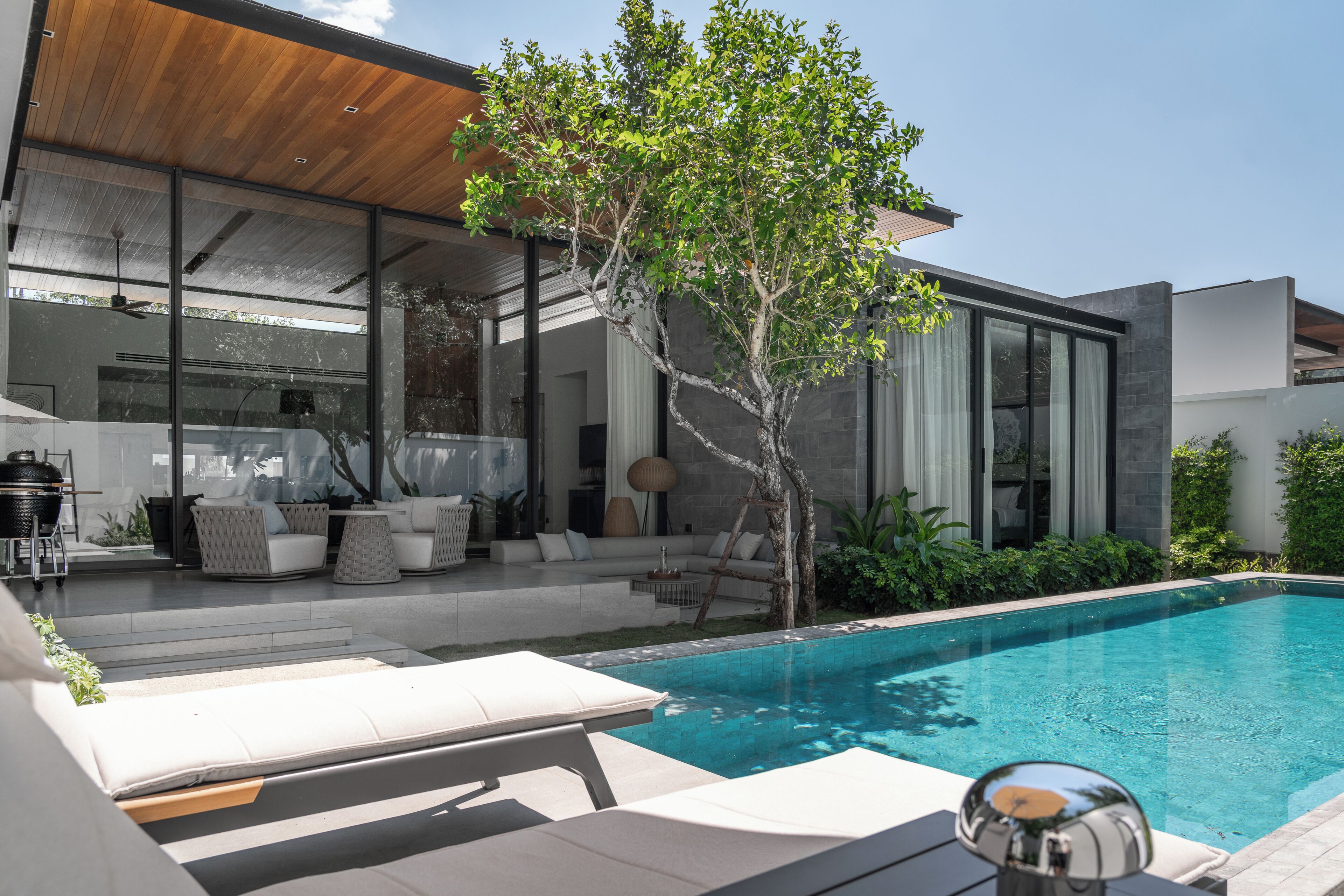 Een modern huis met een zwembad, terras en een boom.