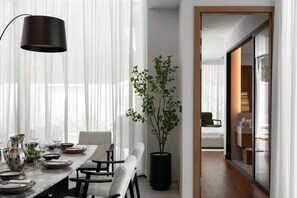 A modern dining area with a table set for two, a potted plant, and a view into another room. - Layan - Private Designer Villa (Tambon Thep Krasatti)