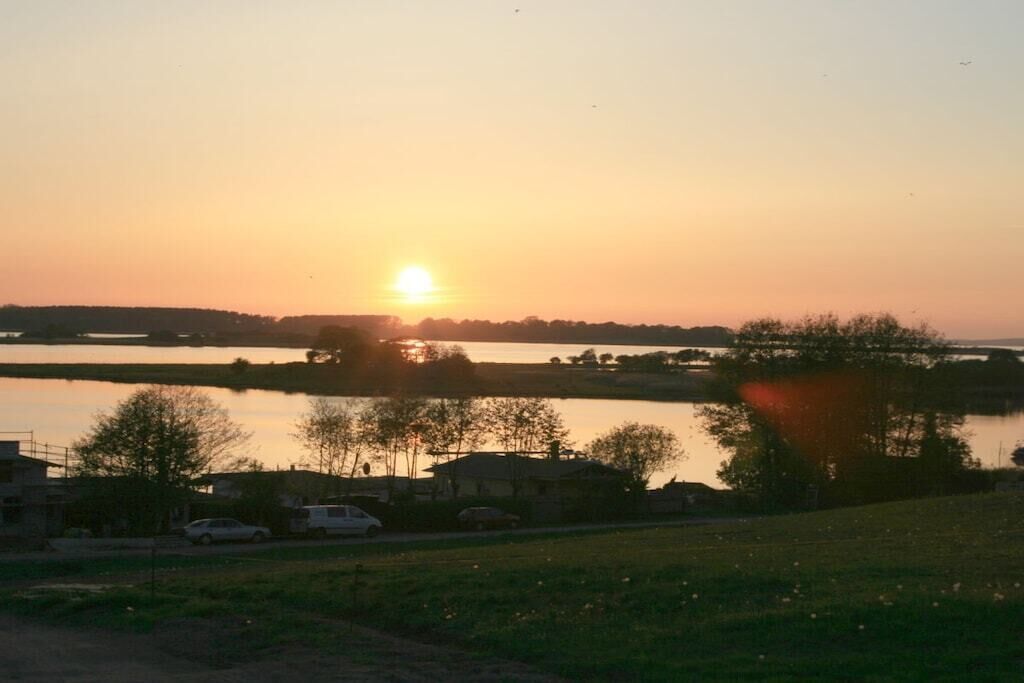 A sunset over a body of water with buildings and trees in the foreground.