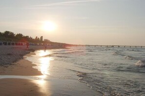 A beach with a pier extending into the water, a clear sky, and the sun low on the horizon. - Jacky's Holiday Apartment 2 (Zinnowitz)