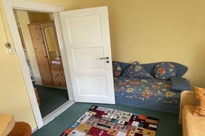 A bedroom with a bed, a door, a wooden wardrobe, and a colorful quilt on the floor. - Jacky's Holiday Apartment 2 (Zinnowitz)