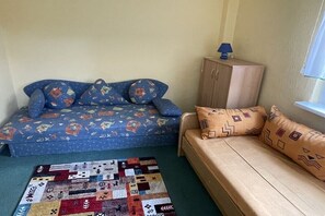 A room with a blue sofa with patterned cushions, a beige sofa with patterned cushions, a small cabinet with a lamp, and a patchwork rug. - Jacky's Holiday Apartment 2 (Zinnowitz)