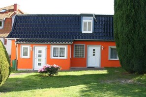 A two-story house with a dark blue tiled roof, orange walls, and white-framed windows. - Jacky's Holiday Apartment 2 (Zinnowitz)
