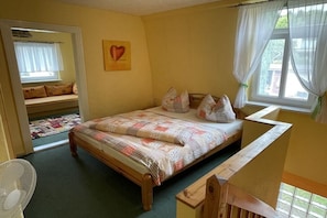 A bedroom with a bed, a window with curtains, a wall with a heart-shaped decoration, and a view of the outside. - Jacky's Holiday Apartment 2 (Zinnowitz)