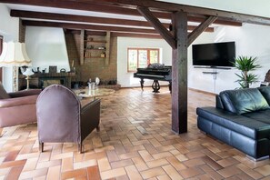 Un salon avec un parquet en point de Hongrie, un piano, une télévision et un canapé.