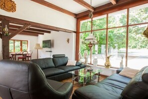 A living room with a sofa set, a coffee table, and a television. There is a window with a view of greenery outside.