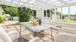 A covered patio with a glass table, wicker chairs, and a view of the garden.
