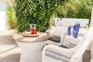 Un espace extérieur aménagé avec des chaises en osier et une table ronde, le tout entouré de verdure.