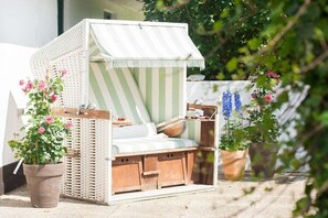 A wicker daybed with a striped canopy, surrounded by potted plants.