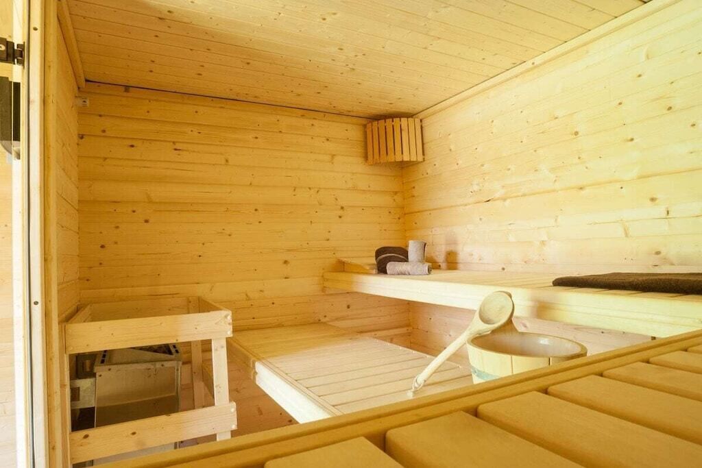 A wooden sauna room with benches, a shelf with towels, and a small wooden structure.