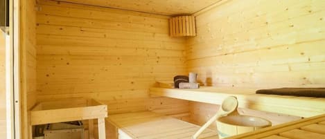 Une salle de sauna en bois, avec des bancs, une étagère pour les serviettes et une petite structure en bois.