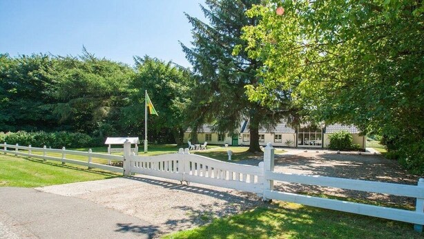 A gated entrance with a white picket fence, a flag, and a building with a tiled roof.