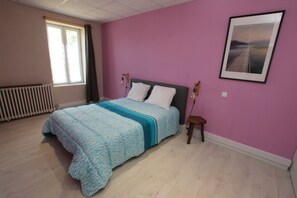 Ein Schlafzimmer mit Bett, Fenster, Heizkörper und einem gerahmten Bild an der Wand.
