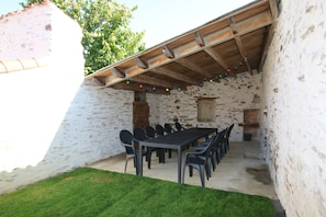 Un espacio de comedor al aire libre rústico, con pared de piedra, techo de madera y una larga mesa con sillas.