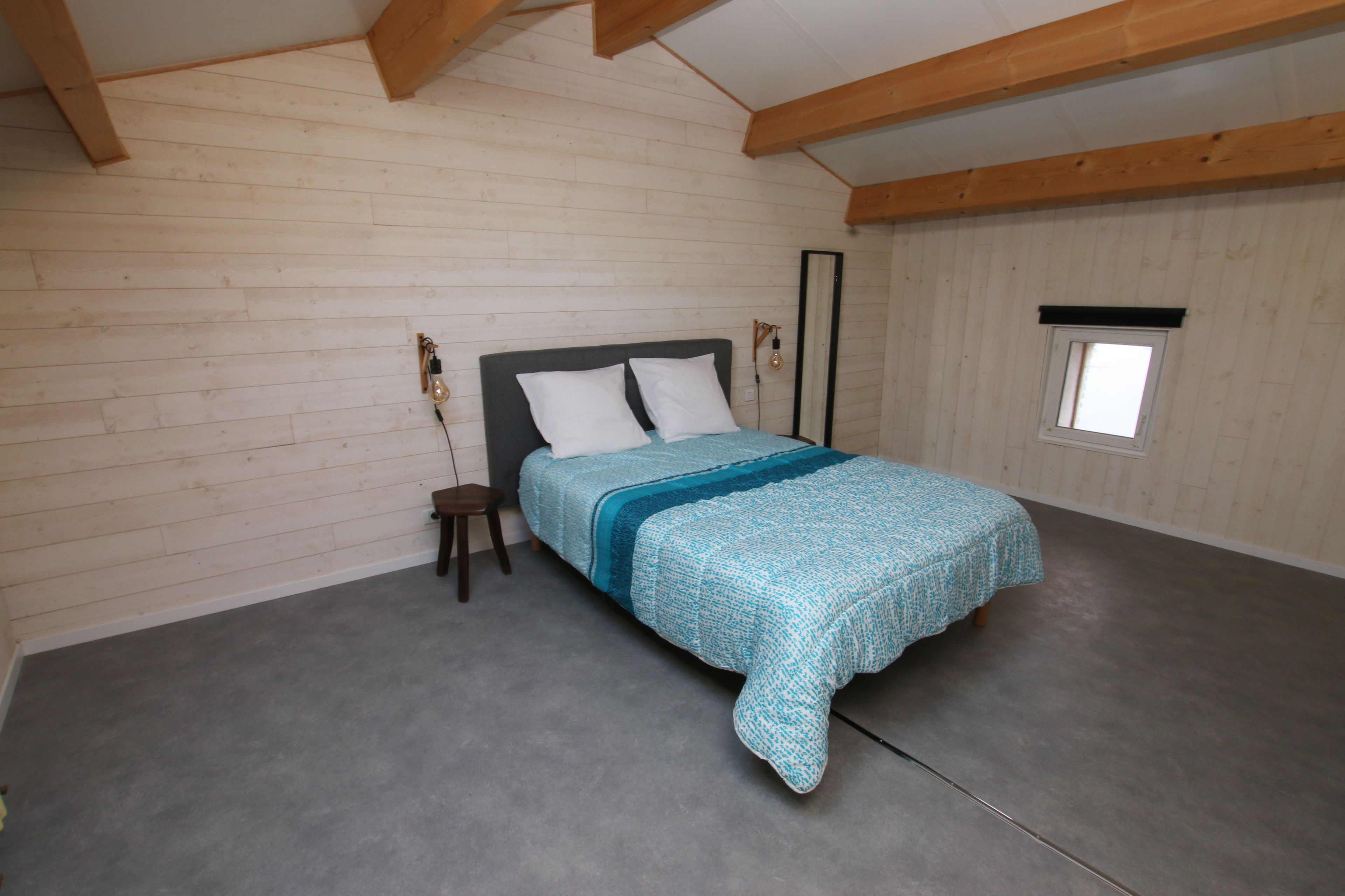 Een slaapkamer met een bed, houten balken, een klein raam en een nachtkastje.