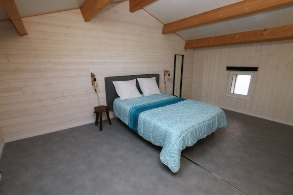 A bedroom with a bed, wooden beams, a small window, and a nightstand.