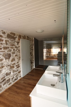 Un baño moderno con pared de piedra, suelo de madera y un espejo grande.