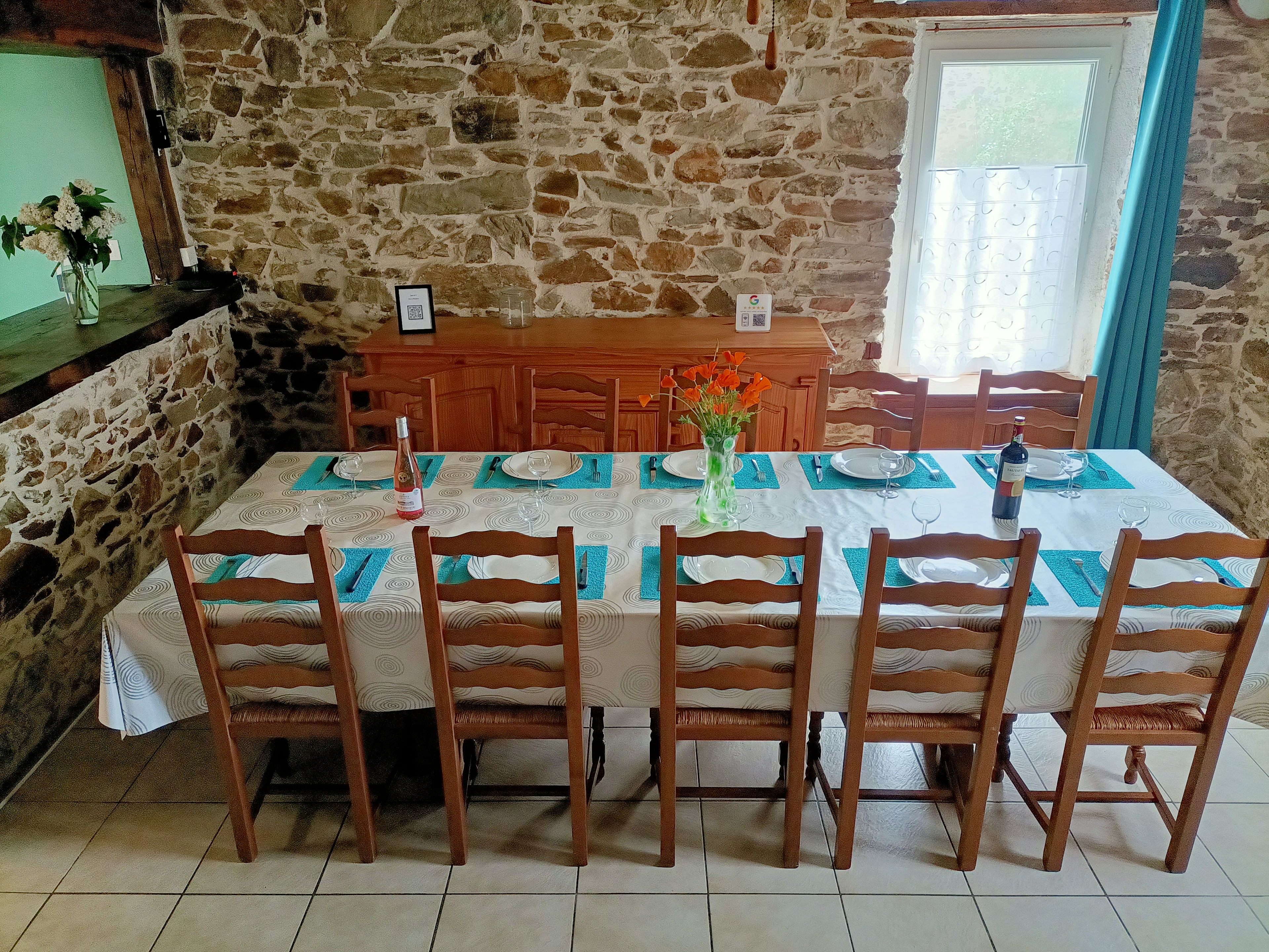 Una mesa de comedor lista con sillas, un jarrón con flores y una botella de vino.