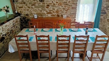 Una mesa de comedor lista con sillas, un jarrón con flores y una botella de vino.